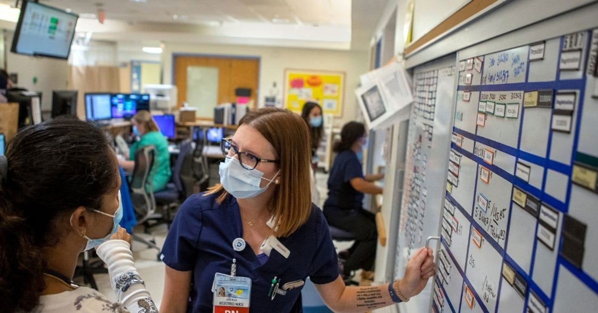 A nurse wearing blue scrubs speaks to a woman. 